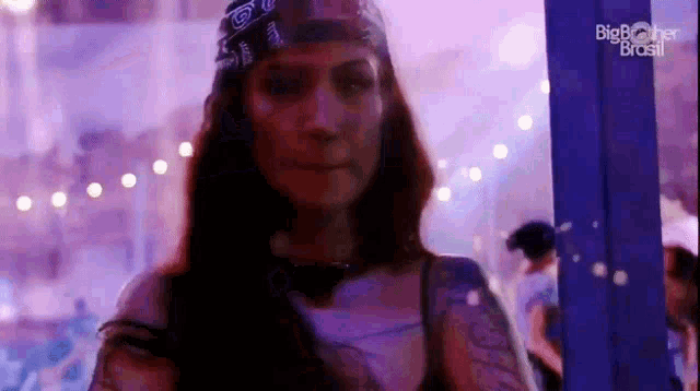 a woman wearing a bandana and a tattoo is standing in front of a purple light .
