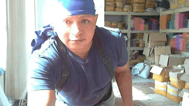 a man wearing a blue shirt and a blue bandana is standing in front of a shelf full of boxes