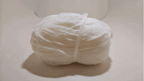 two balls of yarn one green and one white with a frog on top