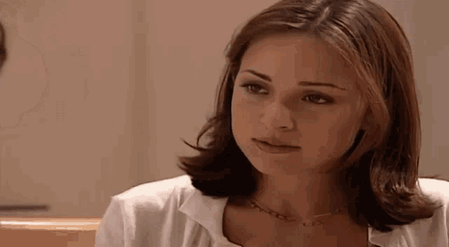 a woman with short brown hair is wearing a white shirt and a gold necklace .