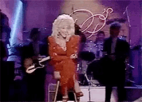 dolly parton is sitting on a stool while playing a guitar on stage