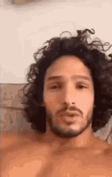 a man with curly hair and a beard is without a shirt .