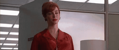 a woman in a red shirt is standing in a hallway in front of a window .