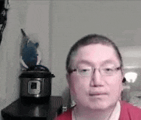 a man wearing glasses and a red shirt is standing in front of a pot on a table .