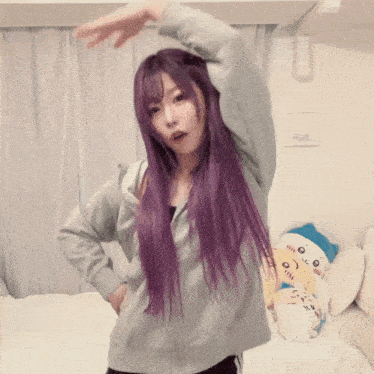 a woman with purple hair is standing in front of a bed with stuffed animals on it