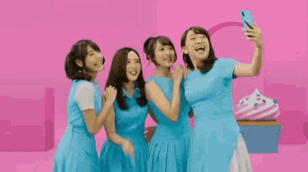four women in blue dresses are taking a selfie together .