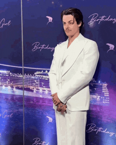 a man in a white suit is standing in front of a birthday sign