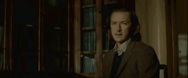 a man in a suit is sitting in front of a bookshelf