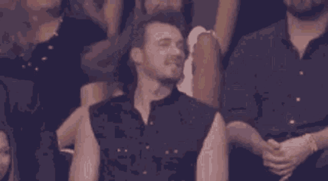 a group of people are sitting in a stadium and a man is sitting in the audience with his eyes closed .