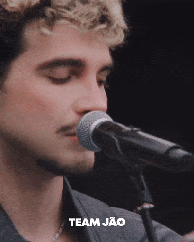a close up of a man singing into a microphone with the word team jao on the bottom right