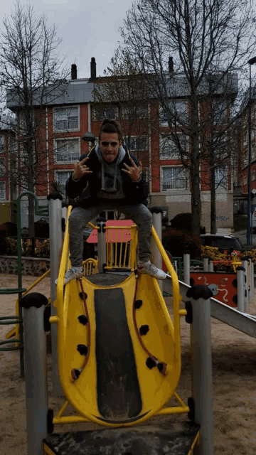 a young man is sitting on a slide at a playground and giving a peace sign