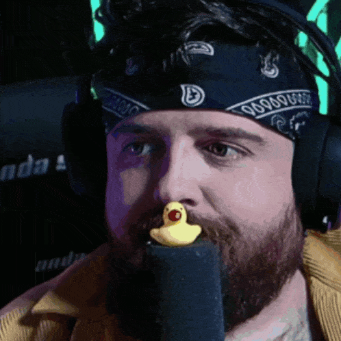 a man wearing headphones and a bandana has a yellow rubber duck in his mouth