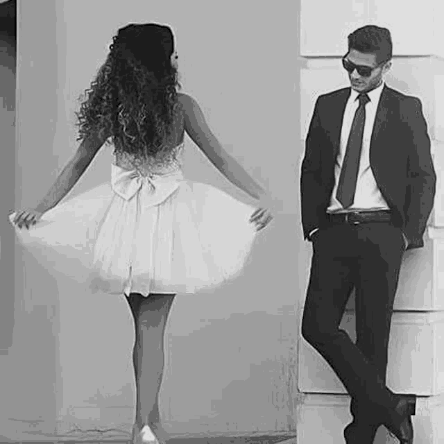 a black and white photo of a man and a woman standing next to each other . the woman is wearing a white dress .