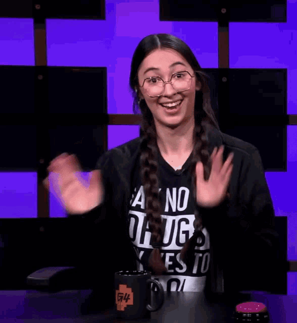 a woman wearing a shirt that says " a no drugs " waves her hands