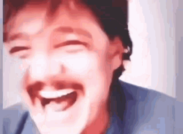 a man with a mustache is laughing with his mouth open in a blurry photo .