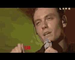 a close up of a man singing into a microphone with the word live in the corner