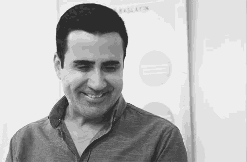 a man is smiling in a black and white photo while standing in front of a sign .