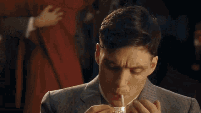 a man in a suit is smoking a cigarette in a dark room
