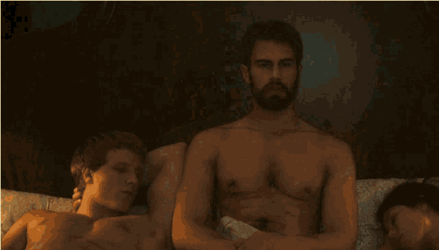 a shirtless man stands in front of a woman laying in bed