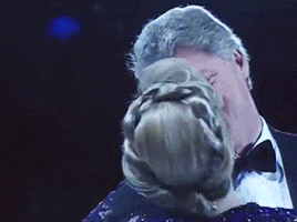 a man in a tuxedo and bow tie is kissing a woman in a blue dress