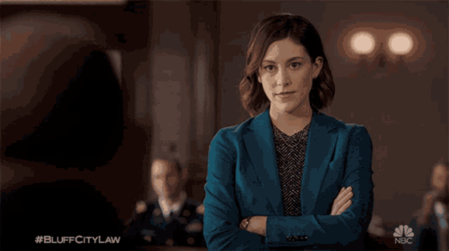 a woman in a blue suit is standing with her arms crossed in front of a nbc sign