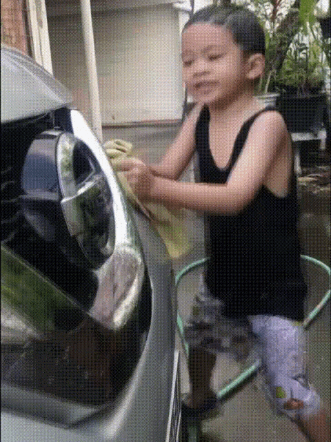 a young boy is washing a car with a towel and a hose