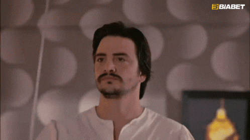 a man with a beard wearing a white shirt with a biabet logo in the background