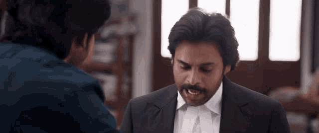 a man in a suit and tie is talking to another man in a blue shirt