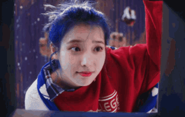 a woman with blue hair and a red sweater is looking out a window .