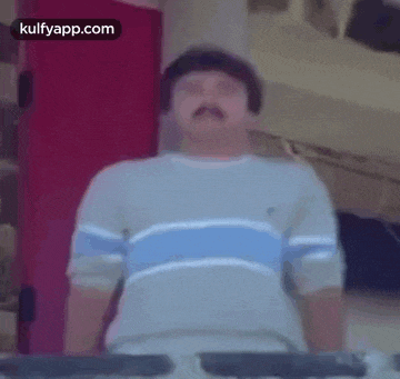a man with a mustache is standing in front of a red door and a keyboard .