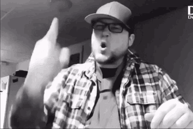 a man wearing glasses and a plaid shirt is giving a middle finger .