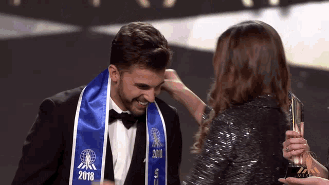 a man is wearing a blue sash that says 2018 on it