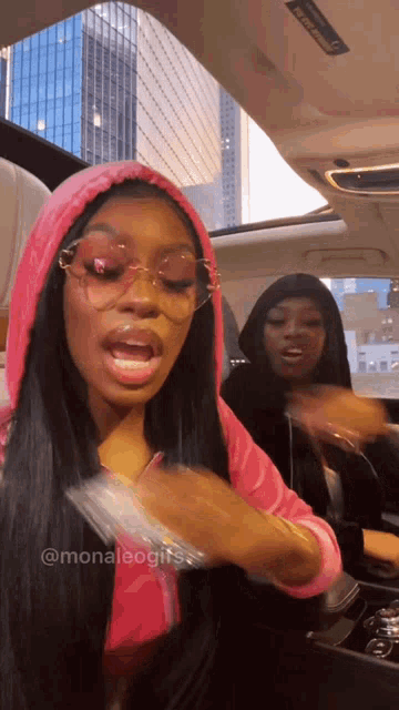 a woman wearing sunglasses and a pink hoodie is sitting in the back seat of a car