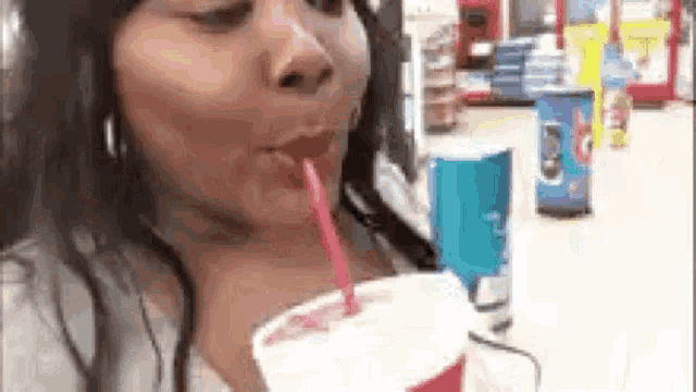 a woman is drinking a milkshake with a straw in a restaurant .