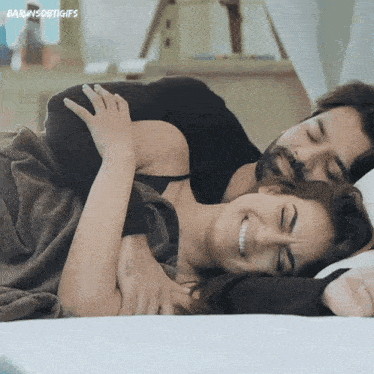 a man and a woman are laying on a bed hugging and smiling .