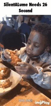 a child is sitting at a table eating a piece of chicken .