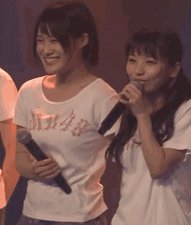 a woman holding a microphone next to another woman wearing a shirt that says m48
