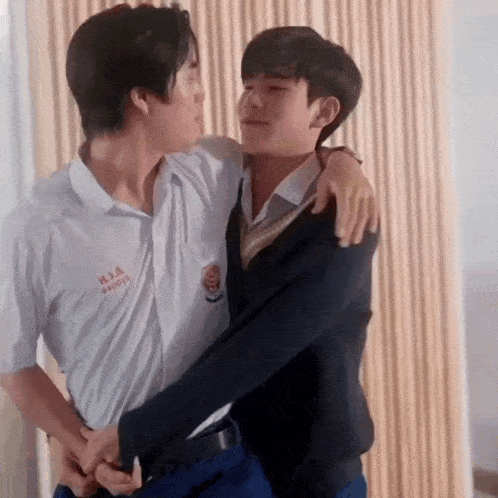 two young men in school uniforms are hugging each other and looking at each other .