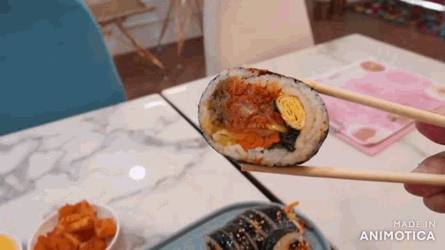 a person is holding a piece of sushi with chopsticks and the words made in animatica are visible