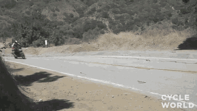a person riding a motorcycle down a road that says cycle world on the side