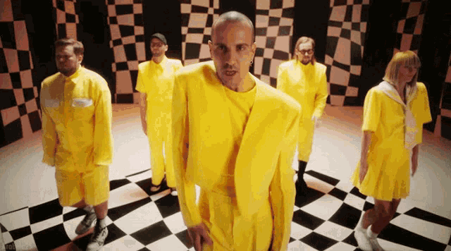 a group of people wearing yellow jumpsuits are standing in a checkered room