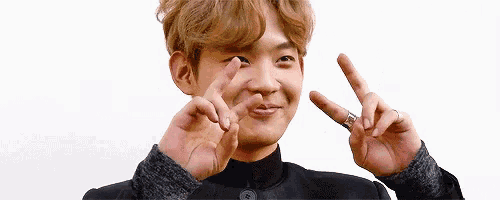 a young man is making a peace sign with his hands while wearing a ring .