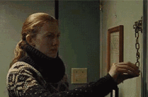 a woman in a sweater is opening a door with a chain around it .