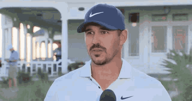 a man wearing a blue hat and a white shirt is talking into a microphone .