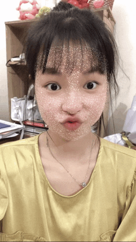 a girl wearing a yellow shirt and a necklace makes a funny face