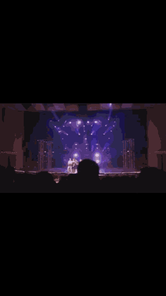 a group of women are dancing on a stage with purple lights behind them