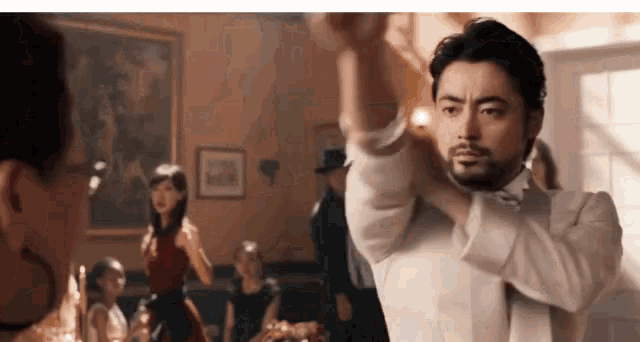 a man in a tuxedo is dancing with a woman in a red dress behind him