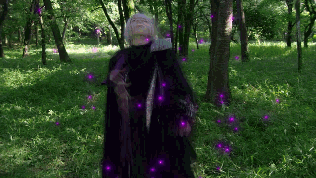 a woman in a black cape stands in a forest with purple lights around her