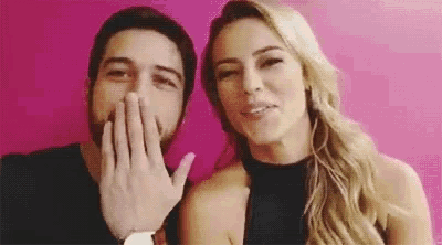 a man and a woman are standing next to each other and the woman is covering the man 's mouth with her hand .