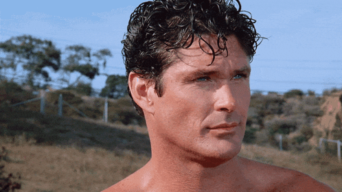 a shirtless man with curly hair looks to his left